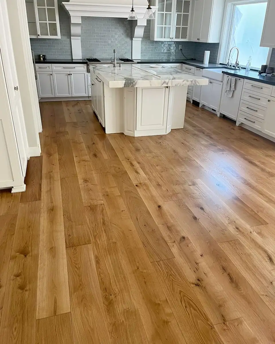 Wide-plank oak flooring installation by Brenham, TX company Garibay Flooring Co in a white kitchen with a marble-topped island